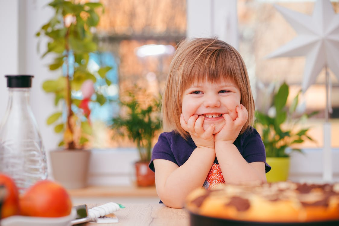 A toddler sitting in a kitchen grinning