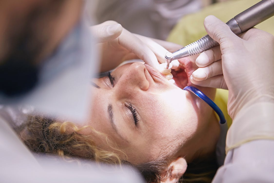 A dentist cleaning a woman’s teeth using a dental drill
